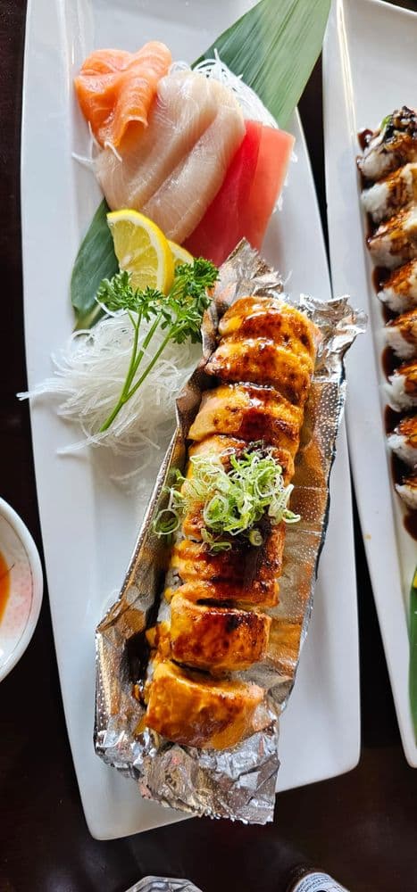 A torched salmon roll plated with a sashimi sampler for catering